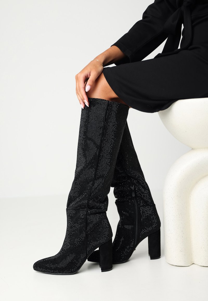 Czarne kozaki do kolan z teksturowanym wzorem, ozdobione małymi ćwiekami. Spiczasty nosek i blokowy obcas, z zamkami błyskawicznymi po bokach.