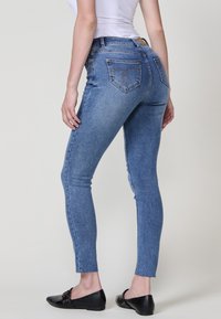 Jean en denim bleu skinny à taille haute, avec des détails légèrement décolorés, deux poches arrière et un ourlet brut. Tissu texturé.