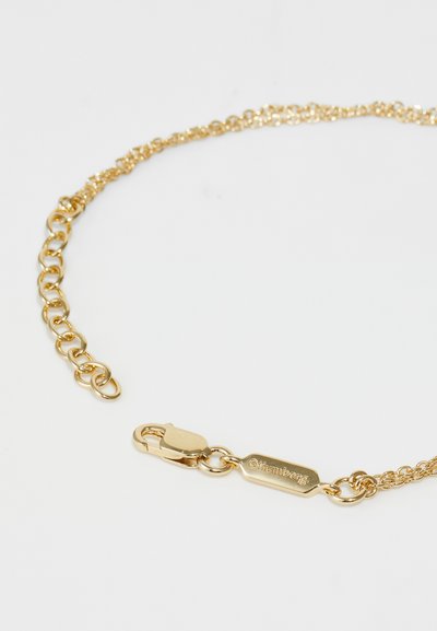 Goldene Kettenarmband mit kunstvollen Gliedern, ausgestattet mit einem Verschluss und einem rechteckigen Anhänger, der mit "triumph" geprägt ist. Glatte Textur und glänzende Oberfläche.