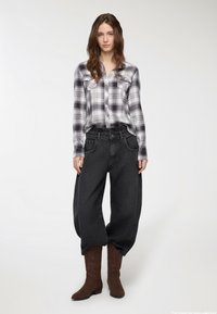 Camicia di flanella a quadri grigia con due tasche sul petto, pantaloni in denim neri oversize e stivali da cowboy ricamati marroni. Dettagli di design e texture semplici.