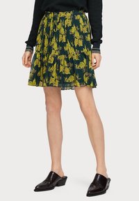 Jupe plissée florale avec un fond vert foncé et des motifs de fleurs jaunes, dotée d'une taille à cordon et d'un ourlet superposé.