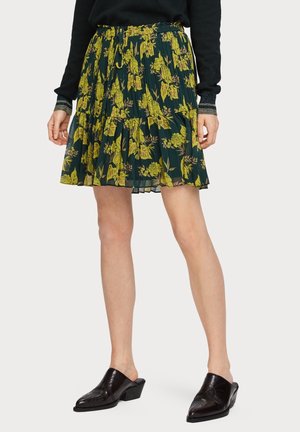 Jupe plissée florale avec un fond vert foncé et des motifs de fleurs jaunes, dotée d'une taille à cordon et d'un ourlet superposé.