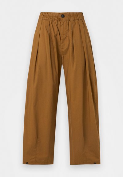 Καφέ παντελόνια σε φαρδιά γραμμή με ελαστική μέση, κούμπωμα με κουμπί, πιέτες στο μπροστινό μέρος και κουμπωμένα ρεβέρ, σε απλό φωτεινό φόντο.