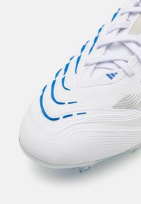 White football boot featuring blue wave patterns, textured surface, and a visible logo. Designed with lace closure and lightweight materials.