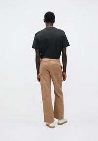 Μαύρο βαμβακερό κοντομάνικο μπλουζάκι και ανοιχτό καφέ φαρδύ παντελόνι cargo με πίσω τσέπες, φορεμένα με μπεζ αθλητικά παπούτσια, εμφανιζόμενα από πίσω σε απλό φόντο.