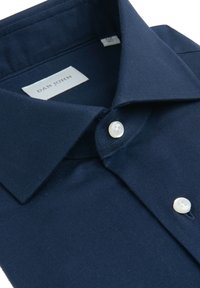 Camisa de vestir azul marino con botones blancos, cuello ancho y etiqueta de la marca Dan John dentro del cuello.