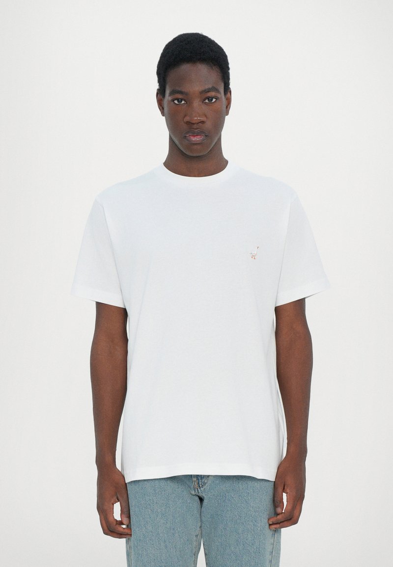 T-shirt en coton blanc à col rond et à manches courtes, présentant un petit design brodé sur le côté gauche de la poitrine.