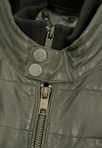 Graue Lederjacke mit Kragen, metallischen Druckknöpfen und einem Reißverschluss. Verfügt über strukturiertes Leder und ein weiches Innenfutter.