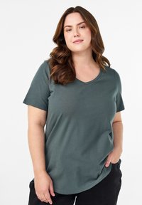 Zelené tričko s krátkým rukávem a véčkovým výstřihem, vyrobené z měkké tkaniny, s volným střihem a zaobleným lemem pro pohodlí a snadné nošení.