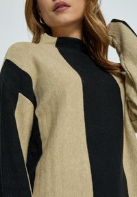Strickpullover mit einem beigen und schwarzen gestreiften Design. Die Textur ist weich, mit einer lockeren Passform und einem hohen Kragen.