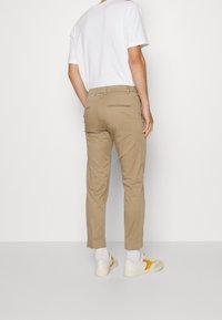 Khaki chinos med slim fit, med en slät yta, bältesöglor, bakfickor och kombinerat med vita sneakers och vita strumpor.