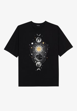 T-shirt noir avec un motif céleste central représentant un soleil avec un visage, des lunes en différentes phases et des étoiles et cercles en orbite.
