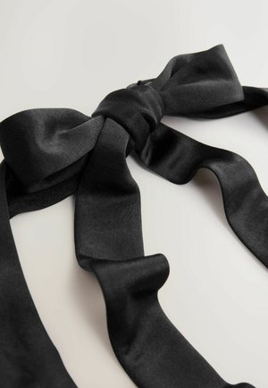 Black satin bow tie with a knot in the center, lying flat with loose ends on a light-colored surface.