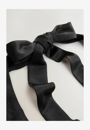 Black satin bow tie with a knot in the center, lying flat with loose ends on a light-colored surface.