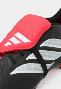 Μαύρο ποδοσφαιρικό παπούτσι με υφή επιφάνειας, επάνω μέρος από ροζ συνθετικό υλικό, έντονο λευκό λογότυπο και μαύρα κορδόνια με γκρι λεπτομέρειες.