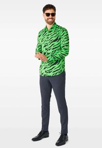 Žalios ir juodos tigro juostelės raštas marškiniai, ilgomis rankovėmis, su apykakle, derinami su tamsiais, tekstūriniais kelniais ir juodais batais.