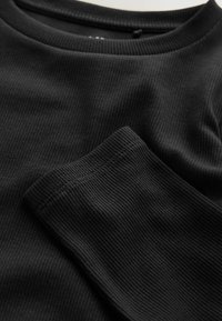 Schwarzes, geripptes Langarmoberteil mit Rundhalsausschnitt und strukturiertem Stoff. Nahaufnahme, die das weiche, dehnbare Material und die Nahtdetails hervorhebt.