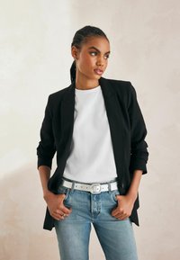 Sort blazer med opfoldede ærmer, hvid t-shirt, lyseblå jeans og sølvbælte. Glat stof og skræddersyet design.