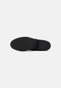 Suela de zapato de cuero negro, diseño plano sin patrón visible, textura suave y acabado mate. El nombre de la marca está grabado en el lado.