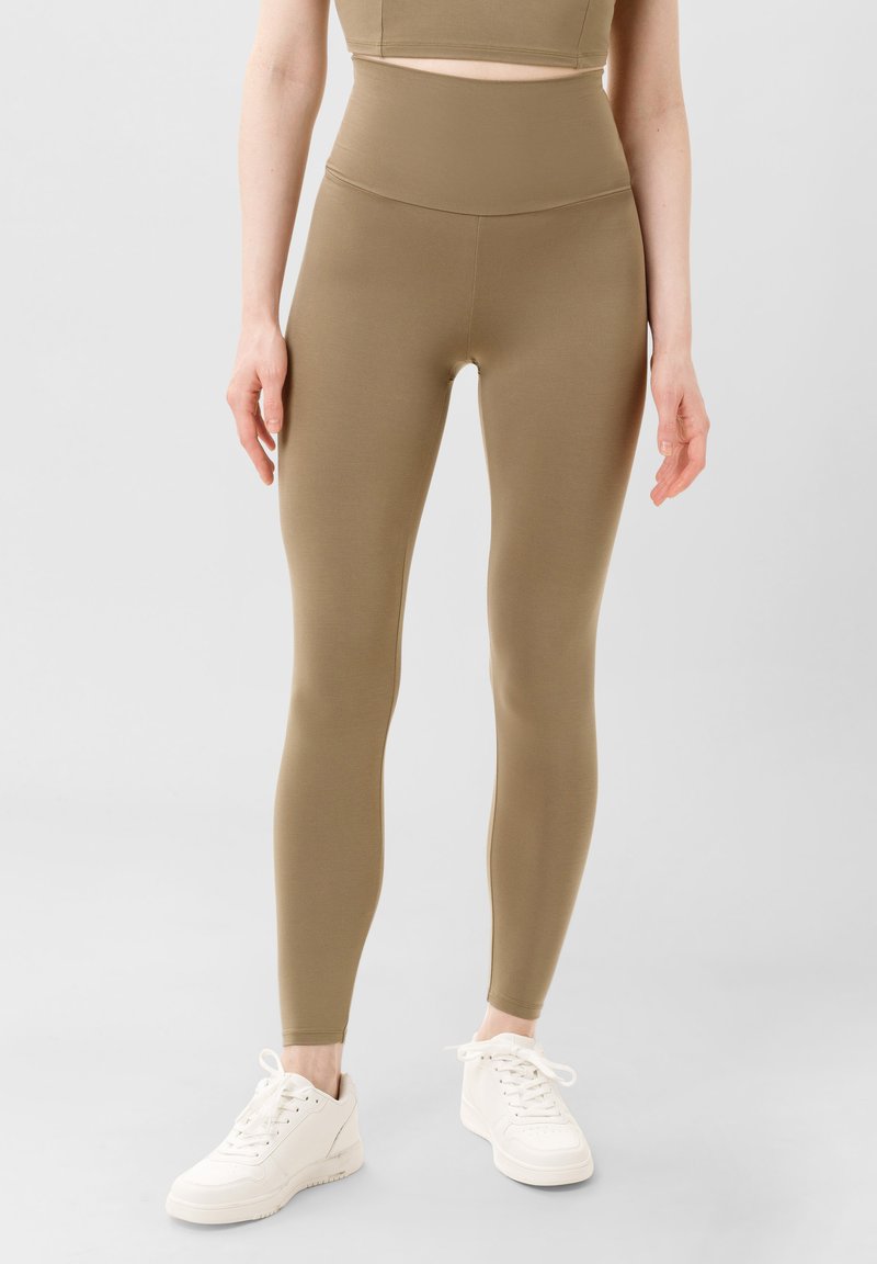 Zelené legíny s vysokým pasem vyrobené z hladkého, elastického materiálu. Mají elegantní design a skvěle se hodí k bílým teniskám.