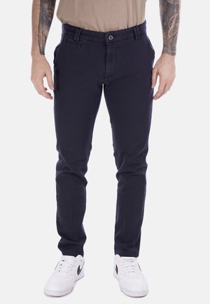 Chinos blu navy realizzati in tessuto misto cotone, con chiusura a bottone, tasche frontali e una vestibilità slim. Indossati con sneakers bianche.