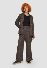 Bruin geruite pak met een losvallende blazer en wijd uitlopende broek. Zwarte geribbelde top eronder, gecombineerd met zwarte schoenen met een dikke zool.