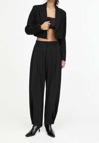 Blazer noir court porté sur un top noir sans bretelles, associé à un pantalon taille haute à jambes larges et des bottines noires à talons pointues.