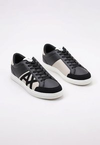 Zapatillas negras y grises con un acabado de cuero suave y ante, que presentan un logotipo blanco contrastante, suela blanca y cordones negros.