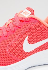 Bright coral Nike running shoe with white swoosh logo, knit upper, coral laces, and padded collar on a white sole.