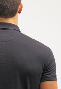 Polo noir à manches courtes, avec un col classique et un tissu lisse et texturé. Vue de l'arrière, montrant des lignes épurées.