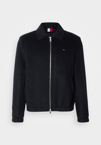 Black zip-up jacket with a collar, featuring side pockets, elastic cuffs, and a small logo patch. Smooth fabric texture.