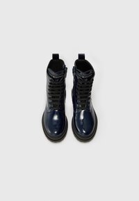 Marina patentsläder ankle boots med svarta snören, gummisula, dragflik bak och logotyp på tungan, som visar en glänsande yta.