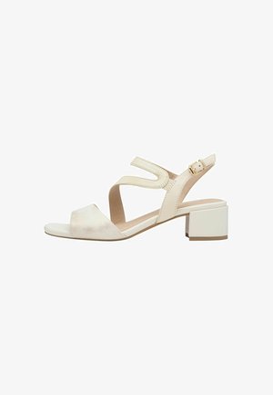 Beige open-te sandal met een middenblokhak, verstelbaar enkelbandje en twee schuine voorbandjes op een witte achtergrond.