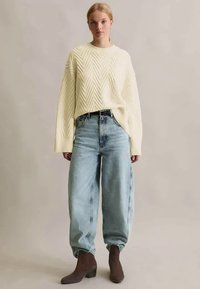 Κρέμα πλεκτό πουλόβερ με σχέδιο ζιγκ ζαγκ, συνδυασμένο με ανοιχτό μπλε φαρδιά τζιν και σκούρα καφέ μποτάκια μέχρι τον αστράγαλο.