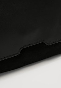 Musta nahkalaukku, jossa on sileä pinta ja hienovarainen, matta viimeistely. Korostettu ompeluyksityiskohdilla ja virtaviivaisella muotoilulla.