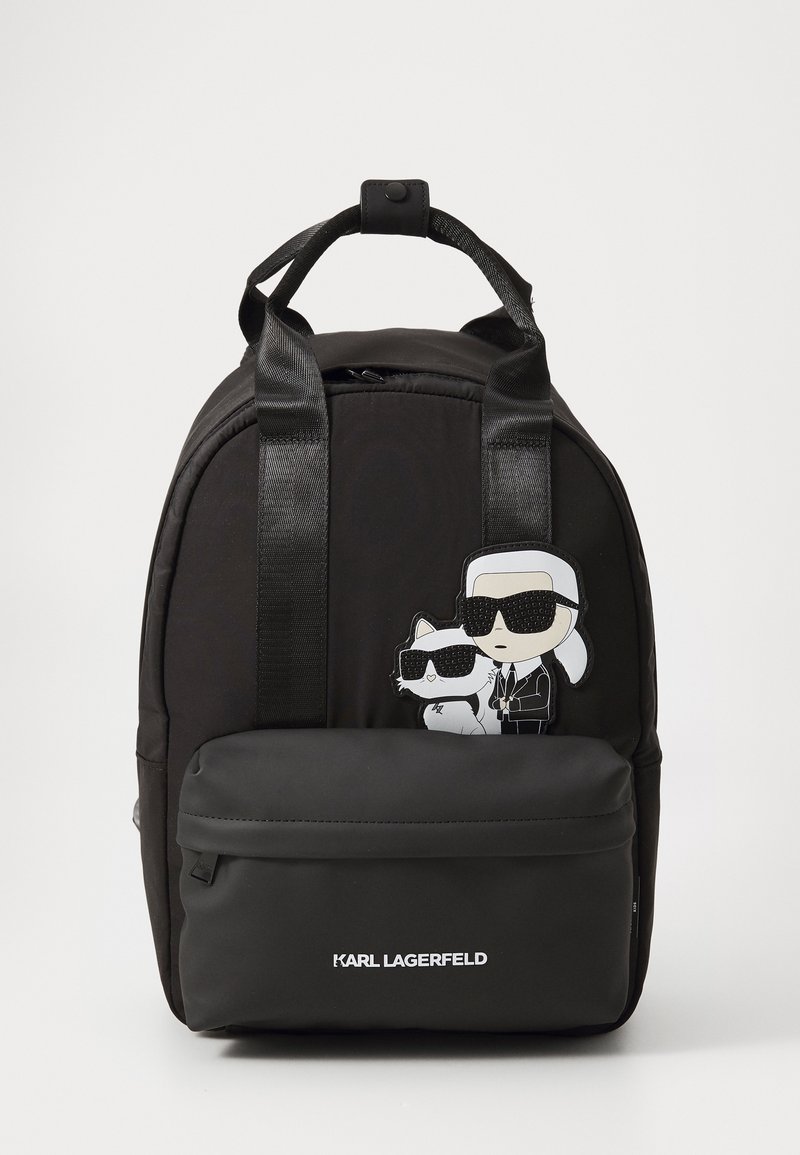 Black nylon backpack with sleek design. Features a front zip pocket and cartoon patch of a figure with sunglasses and a cat. Logo displayed.