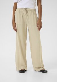 Pantalons large couleur beige avec une taille élastique et un cordon de serrage, dotés de deux poches avant et d'une texture de tissu lisse et légère.