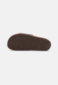 Sola de chinelo de borracha castanha com padrões de aderência circulares, superfície texturizada e uma borda ligeiramente elevada. Design plano e durável para conforto.