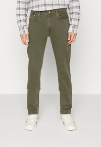 Olivově zelené chinos kalhoty vyrobené z měkkého materiálu, s úzkým střihem, pěti kapsami a zapínáním na knoflík. Ozdobené švy.