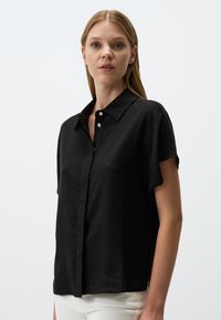 Schwarzes kurzärmliges Hemd aus leichtem Stoff, mit einem Button-down-Kragen und subtiler Textur. Knöpfe vorne; lockere Passform.