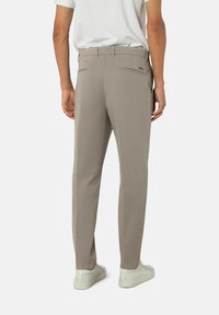 Beige Hose mit schmaler Passform, aus glattem Stoff, mit Gesäßtaschen und einem dezenten Markenanhänger. Kombiniert mit hellen Sneakers.