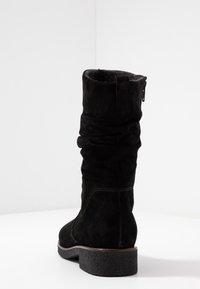 Bottine en suède noire avec un design ample, des accents cousus, un bout rond et un petit talon texturé, agrémenté d'une fermeture éclair sur le côté.