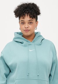 Hoodie azul-turquesa claro com cordões, bolso canguru e logo da Nike em branco bordado no peito. Tecido suave, corte descontraído.