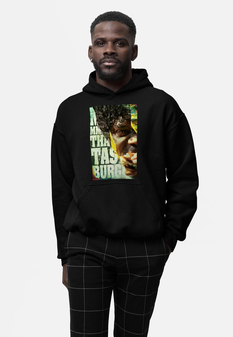 Felpa nera con una grande stampa grafica di un volto e testo. La felpa ha una tasca frontale e un design rilassato. I pantaloni presentano un motivo a griglia bianca.