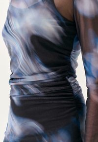 Robe élégante en tissu léger, présentant un motif tourbillonnant bleu et noir avec un ruché à la taille et de longues manches transparentes.
