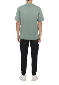 Green cotton T-shirt, short sleeves, crew neckline. Paired with black cargo pants featuring pockets. White sneakers complete the outfit.