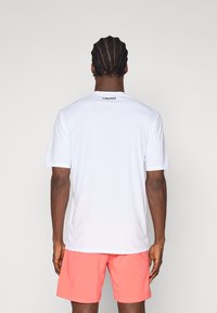 Hvid træningsskjorte med kortærmer og "HEAD" logo på ryggen, kombineret med koralfarvede shorts; glat stof og regular fit.