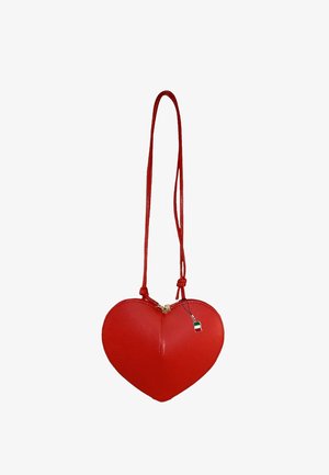 Red leather heart-shaped bag with a zip closure, thin strap, and a small tag featuring a green, white, and red design.
