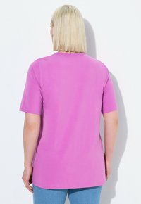 Růžové tričko s krátkým rukávem vyrobené z měkké bavlny, s volným střihem a kulatým výstřihem, vyobrazené ze zadu na bílém pozadí.