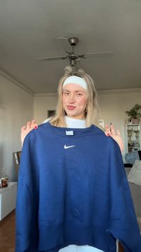 Marinblå oversized Nike-tröja med rund halsringning och vit logotyp. Mjukt tyg med ribbade muddar och nederkant, hålls av en person inomhus.